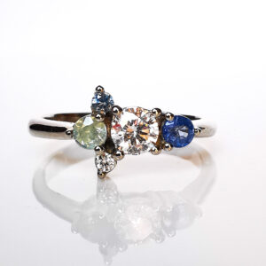 Alt: Anillo de compromiso Fiesta asimétrico en oro blanco paladio con diamante y zafiros fancy